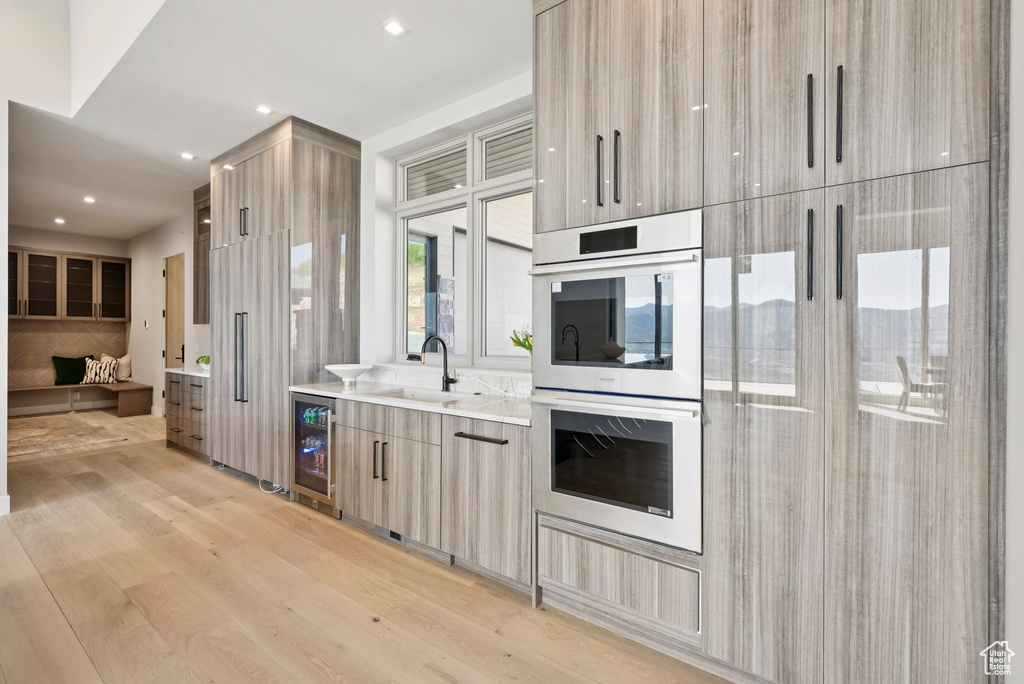 Kitchen with double oven, modern cabinets, light wood finished floors, light countertops, and wine cooler