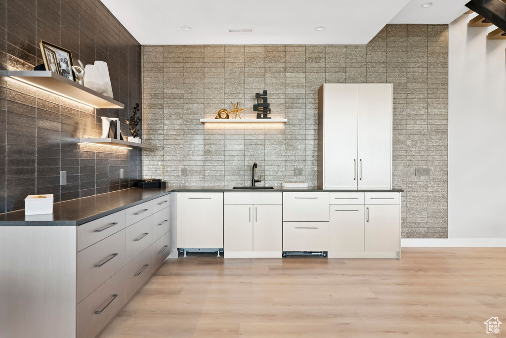 Kitchen with open shelves, dark countertops, light wood-style flooring, and decorative backsplash