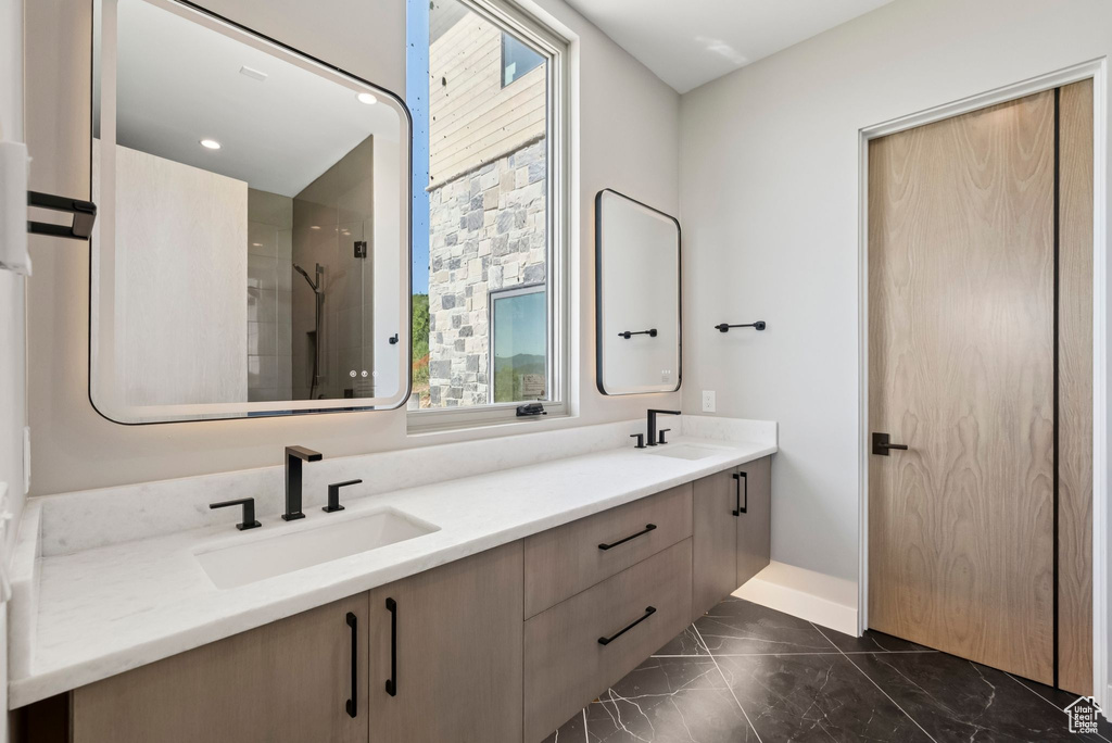 Bathroom with marble finish flooring, double vanity, and a shower