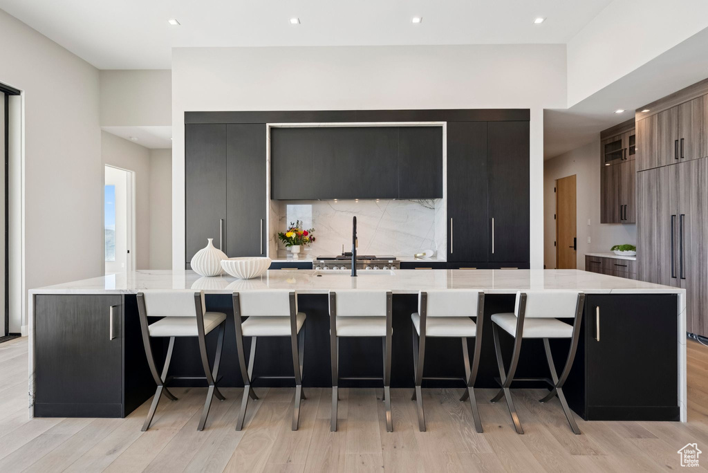 Kitchen with modern cabinets, a large island, light wood-style flooring, tasteful backsplash, and a breakfast bar