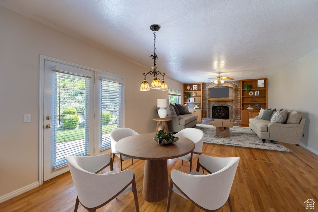 Dining room featuring built in features, a fireplace, light hardwood / wood-style floors, brick wall, and ceiling fan