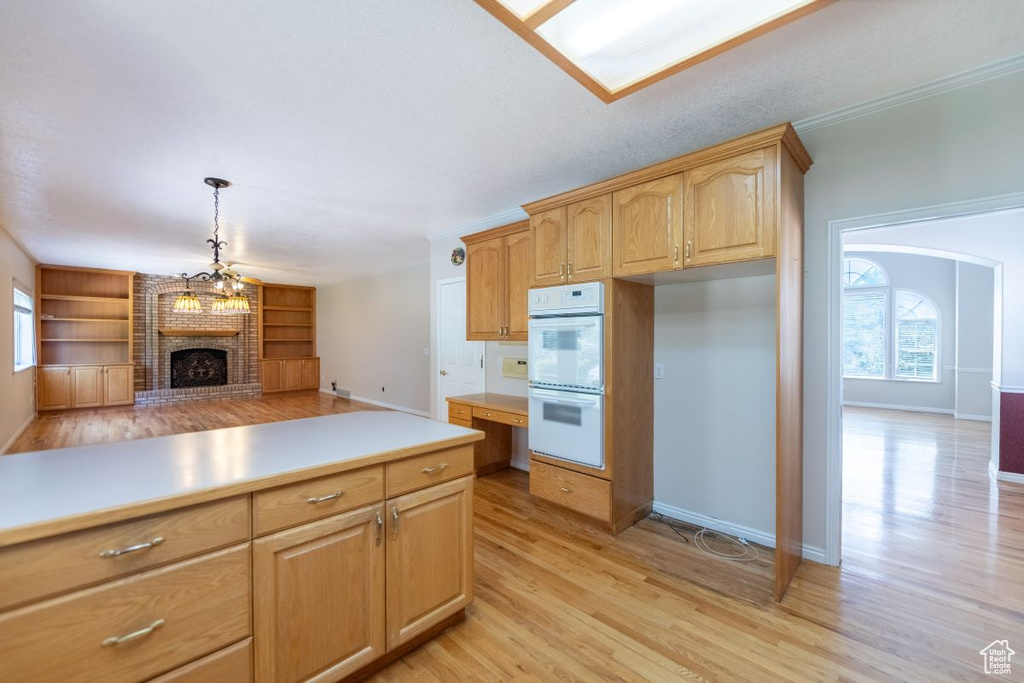 Kitchen with double oven, light hardwood / wood-style floors, a brick fireplace, brick wall, and pendant lighting