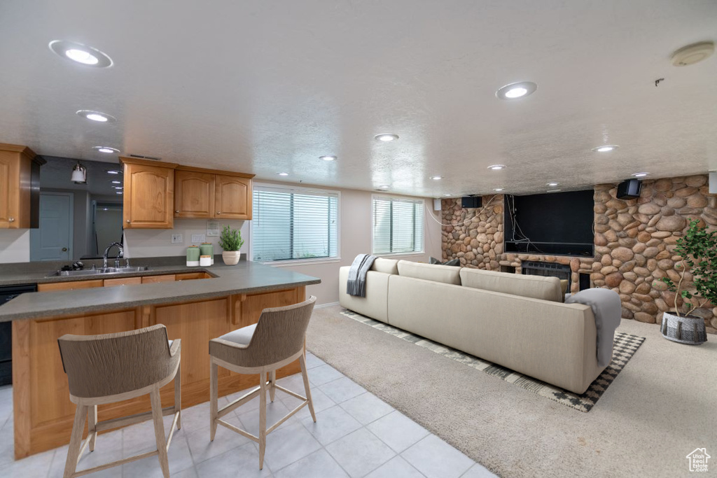 Kitchen featuring a stone fireplace, sink, dishwasher, a kitchen bar, and light tile patterned floors