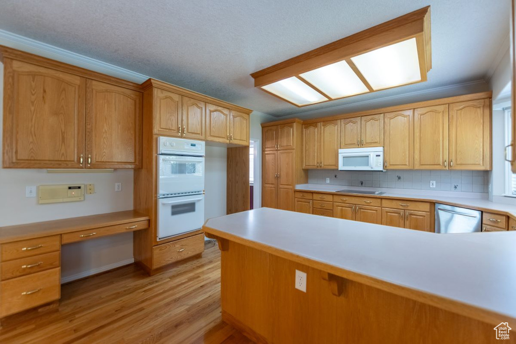 Kitchen with decorative backsplash, crown molding, white appliances, and light hardwood / wood-style floors