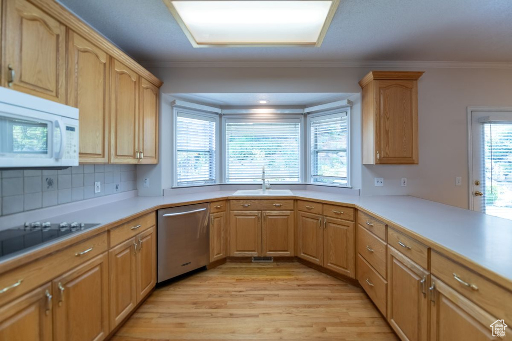 Kitchen featuring tasteful backsplash, ornamental molding, sink, dishwasher, and light hardwood / wood-style flooring