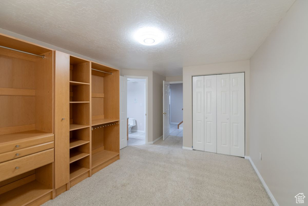 Unfurnished bedroom with two closets, a textured ceiling, light colored carpet, and connected bathroom