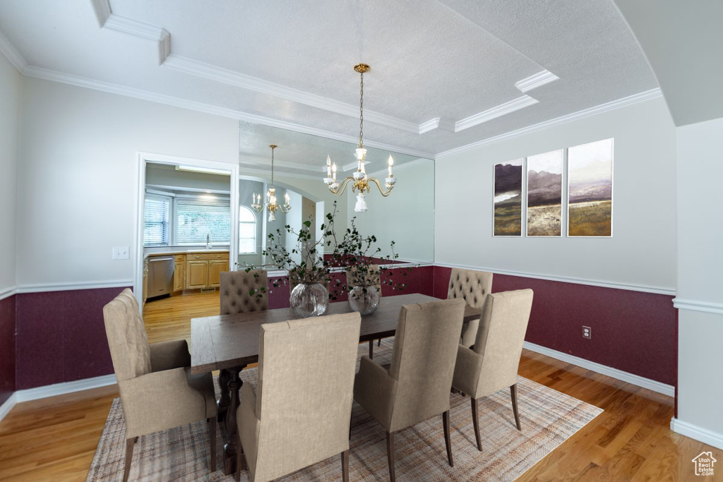 Dining space featuring a chandelier, ornamental molding, a raised ceiling, and light hardwood / wood-style floors