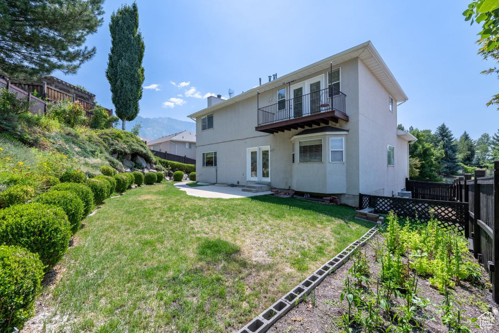 Rear view of property featuring a patio area, a balcony, and a lawn