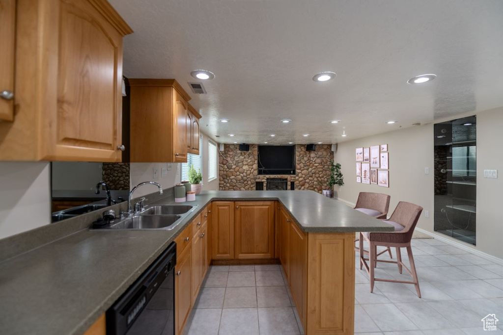 Kitchen with kitchen peninsula, sink, dishwasher, light tile patterned floors, and a kitchen breakfast bar