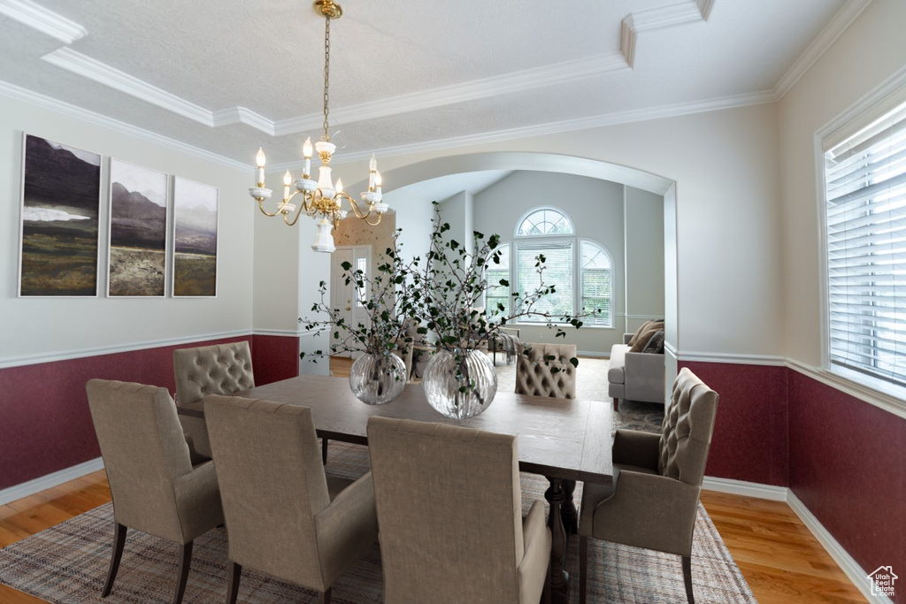 Dining area featuring crown molding, a raised ceiling, light hardwood / wood-style flooring, and a chandelier