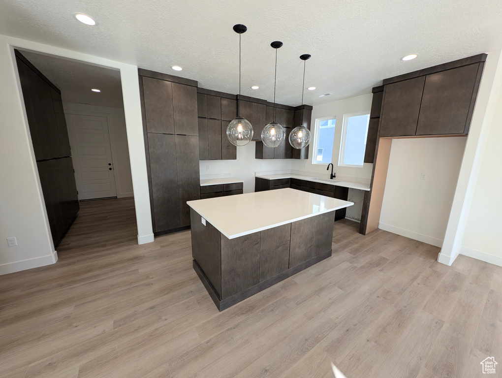 Kitchen featuring sink, a textured ceiling, a center island, light hardwood / wood-style floors, and pendant lighting