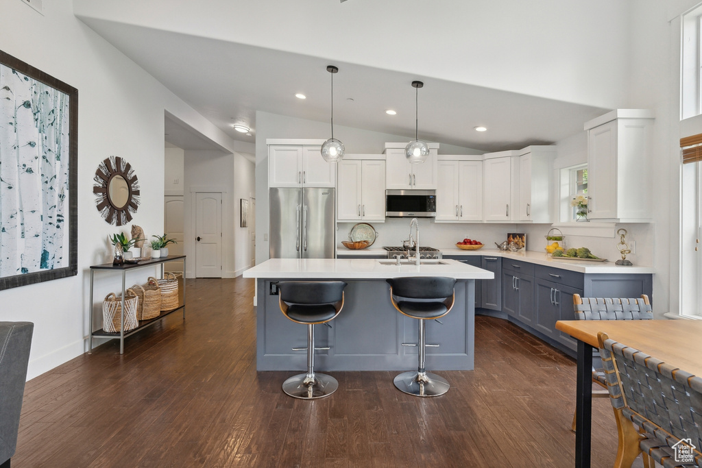 Kitchen featuring hanging light fixtures, dark hardwood / wood-style flooring, white cabinets, a breakfast bar, and appliances with stainless steel finishes