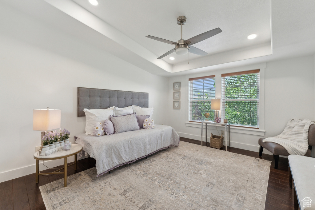 Bedroom with dark hardwood / wood-style floors, ceiling fan, and a raised ceiling