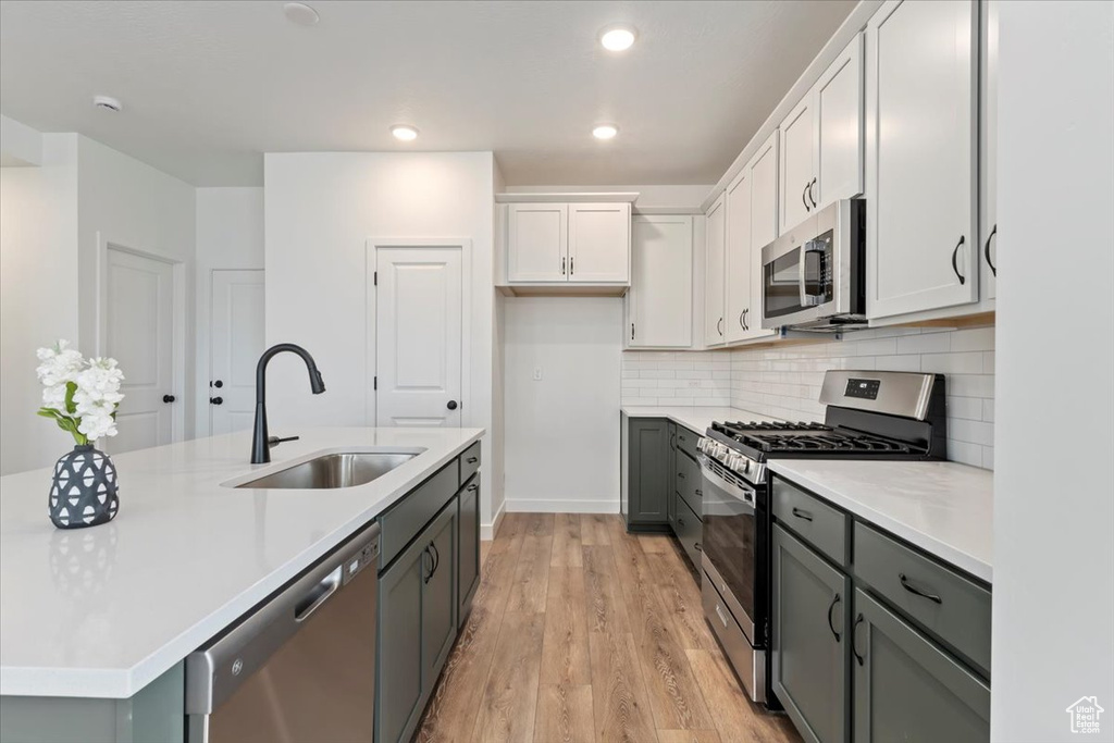 Kitchen with a kitchen island with sink, white cabinetry, light hardwood / wood-style flooring, stainless steel appliances, and sink