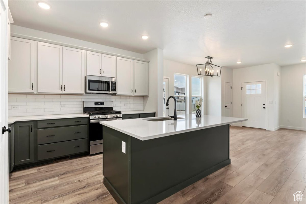 Kitchen with a notable chandelier, light hardwood / wood-style flooring, sink, appliances with stainless steel finishes, and a center island with sink