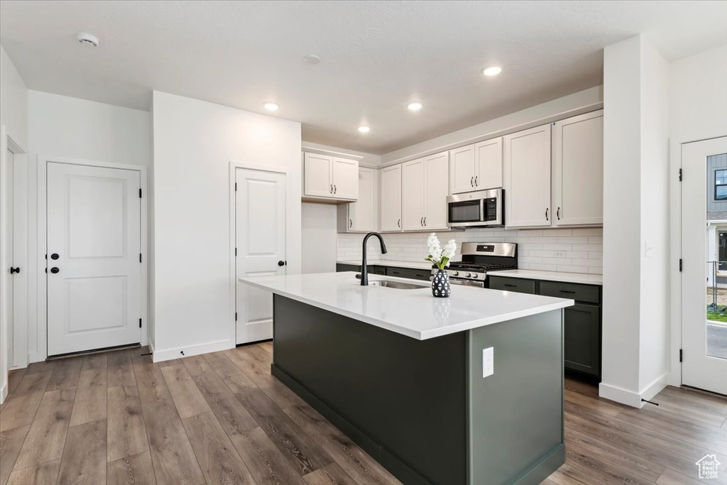 Kitchen with hardwood / wood-style floors, backsplash, stainless steel appliances, sink, and a center island with sink