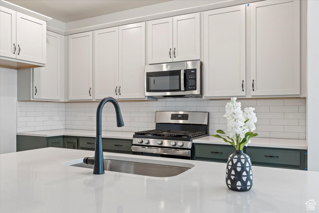 Kitchen featuring stainless steel appliances, sink, decorative backsplash, and white cabinets