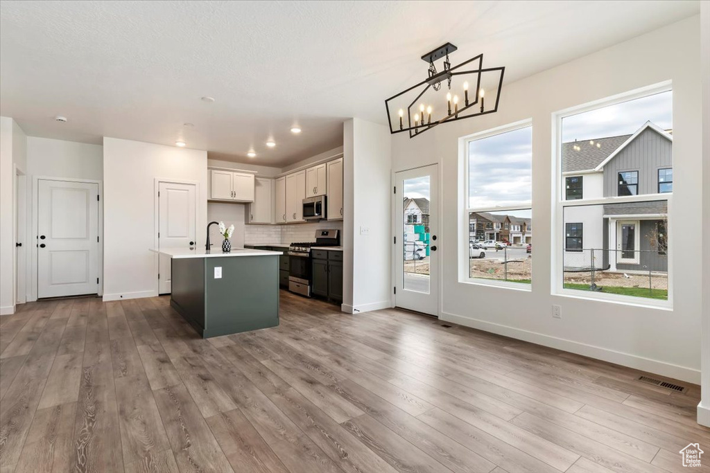 Kitchen with pendant lighting, stainless steel appliances, wood-type flooring, an inviting chandelier, and an island with sink