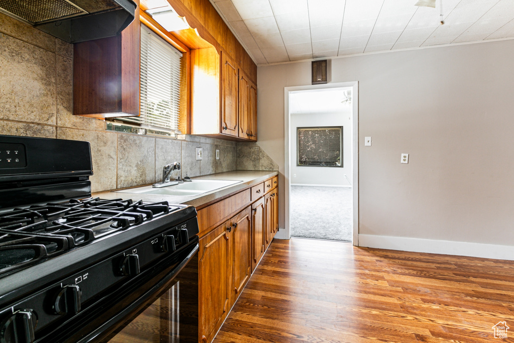 Kitchen with black gas range, backsplash, custom exhaust hood, hardwood / wood-style floors, and sink