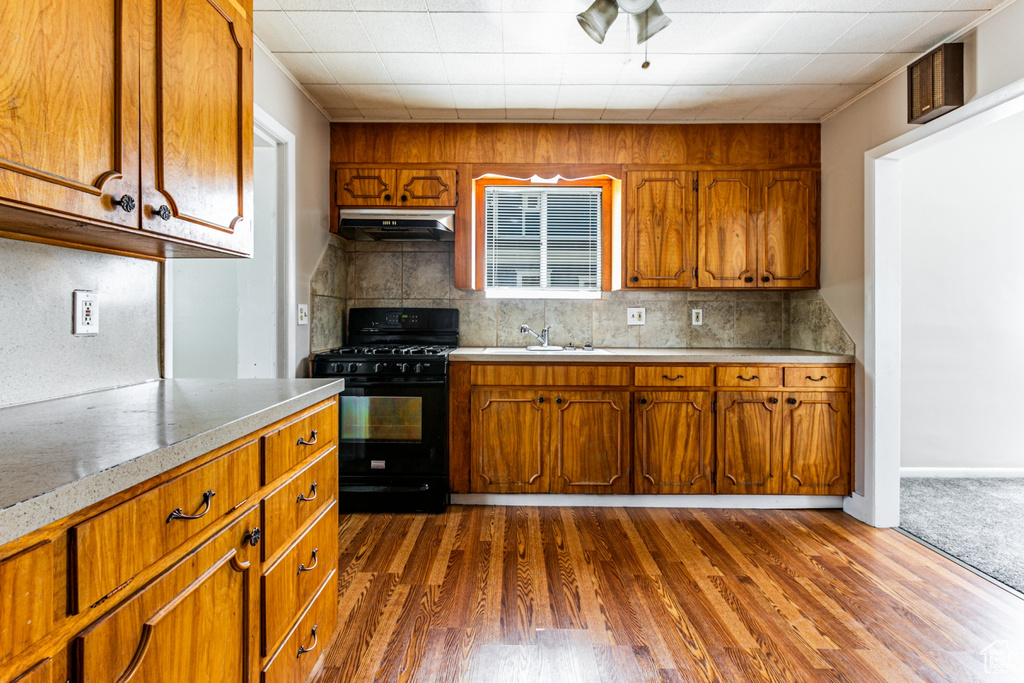 Kitchen with backsplash, dark colored carpet, black range with gas cooktop, range hood, and sink