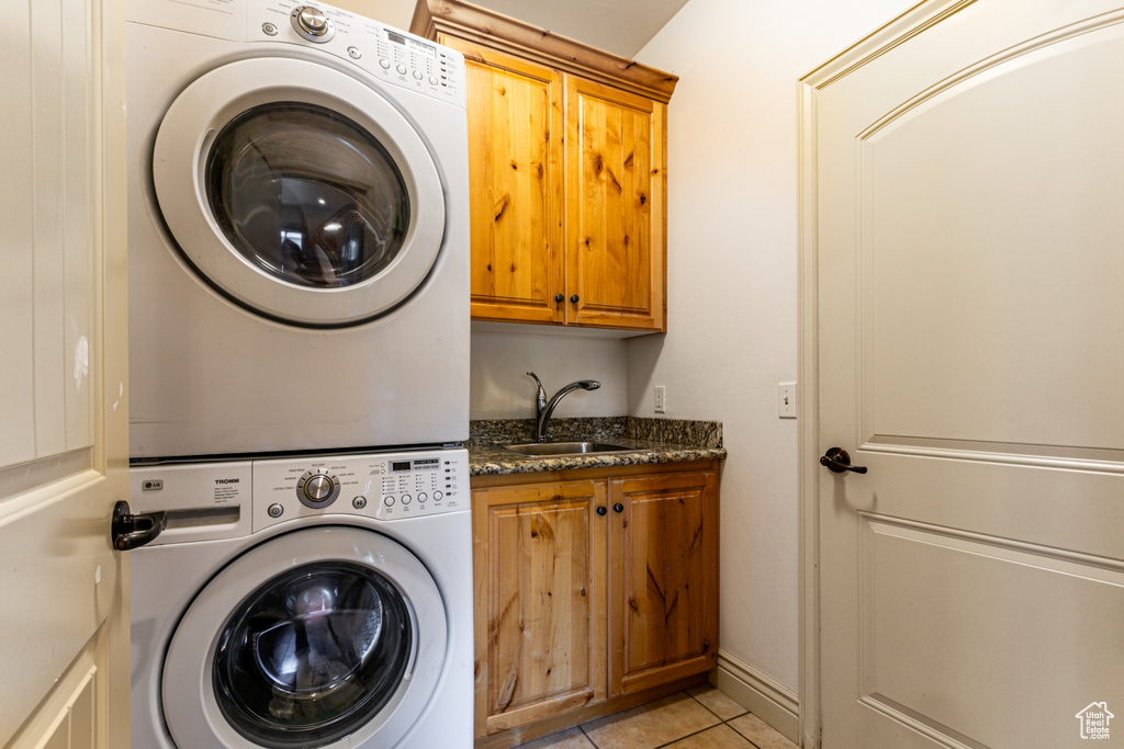 Clothes washing area with light tile patterned flooring, sink, cabinets, and stacked washing maching and dryer