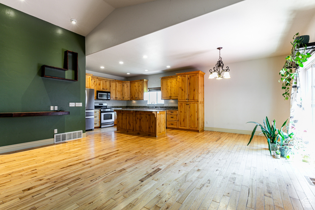 Kitchen featuring stainless steel appliances, light hardwood / wood-style floors, decorative light fixtures, and a kitchen island