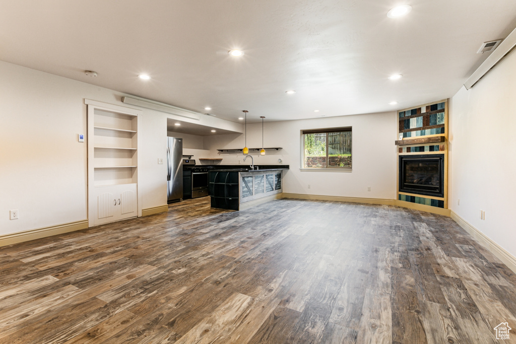 Unfurnished living room featuring sink, built in shelves, and hardwood / wood-style flooring