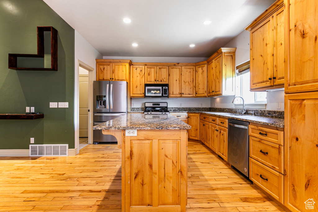 Kitchen with dark stone counters, stainless steel appliances, a breakfast bar, a kitchen island, and light wood-type flooring