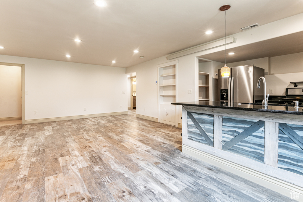 Kitchen featuring dark stone counters, sink, pendant lighting, light hardwood / wood-style floors, and stainless steel refrigerator with ice dispenser