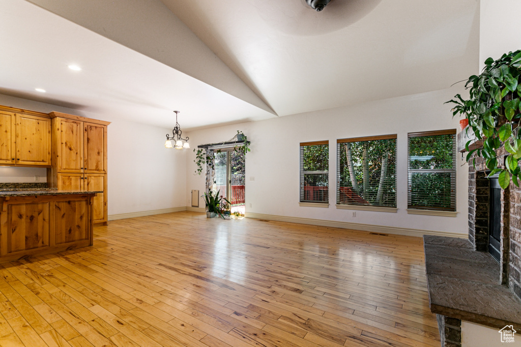 Unfurnished living room featuring lofted ceiling, a notable chandelier, light hardwood / wood-style floors, a fireplace, and radiator