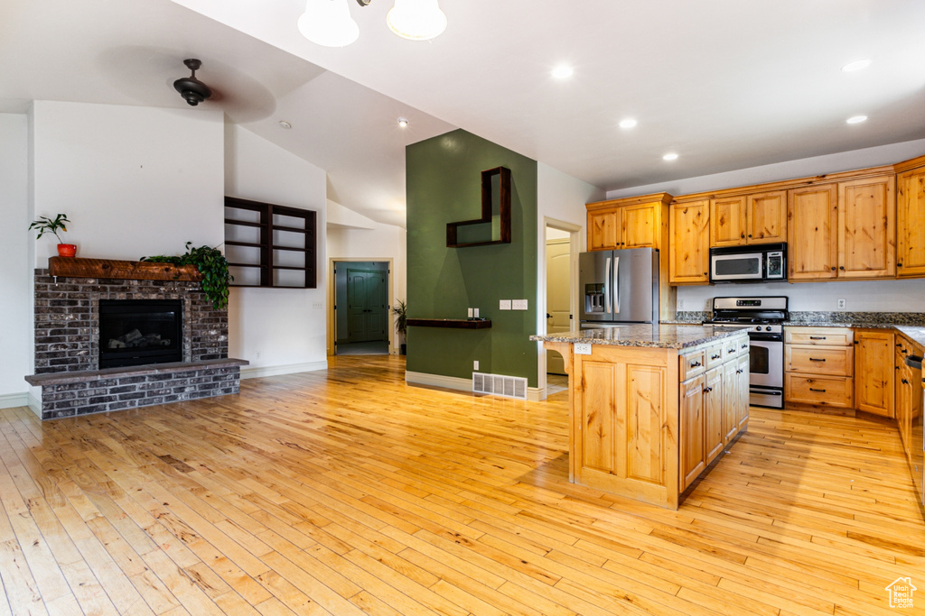 Kitchen with a breakfast bar area, light hardwood / wood-style flooring, a kitchen island, stainless steel appliances, and a brick fireplace