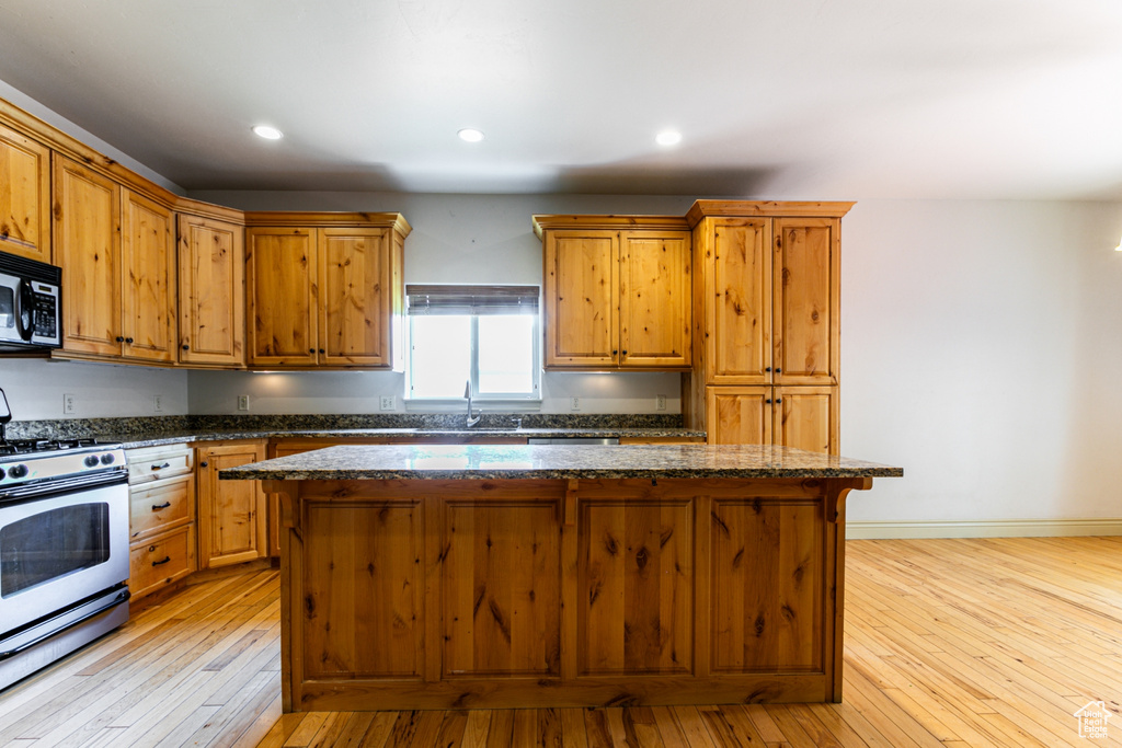 Kitchen with sink, dark stone countertops, double oven range, a kitchen island, and light hardwood / wood-style floors