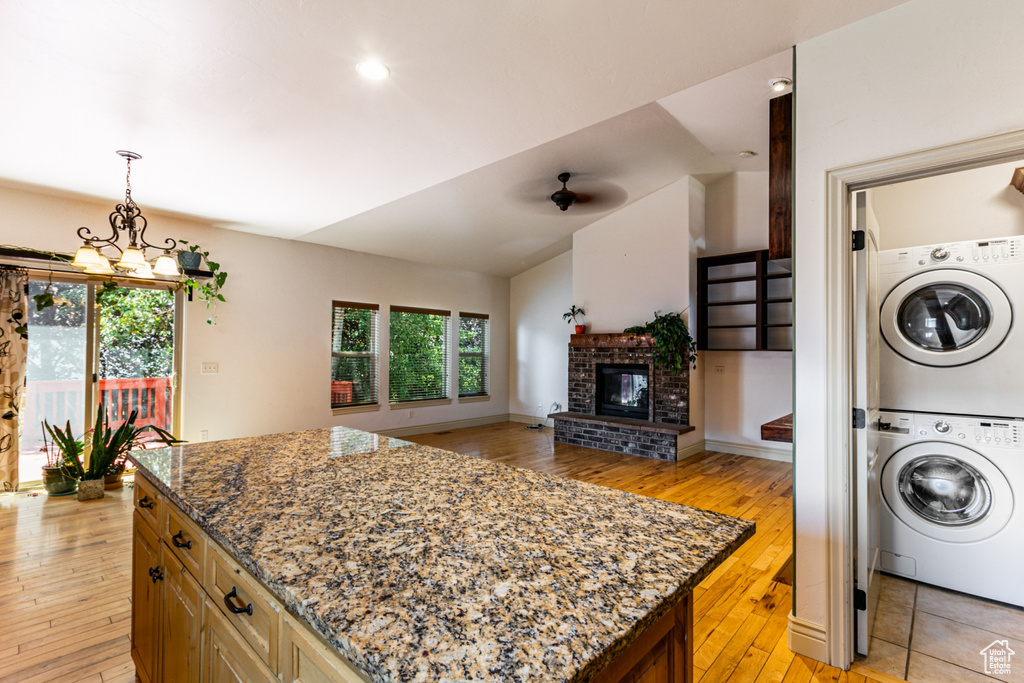 Kitchen with a fireplace, a kitchen island, light wood-type flooring, and stacked washing maching and dryer