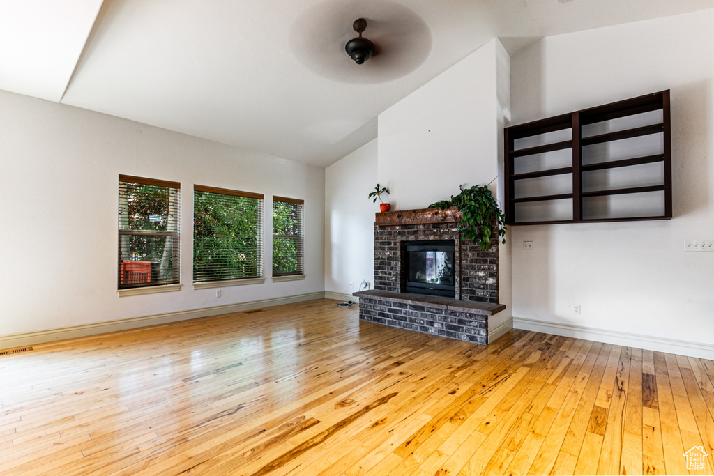 Unfurnished living room featuring light hardwood / wood-style floors, a brick fireplace, ceiling fan, and high vaulted ceiling