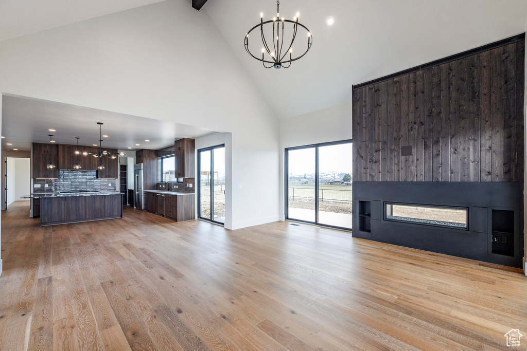 Unfurnished living room with high vaulted ceiling, light wood-type flooring, and an inviting chandelier