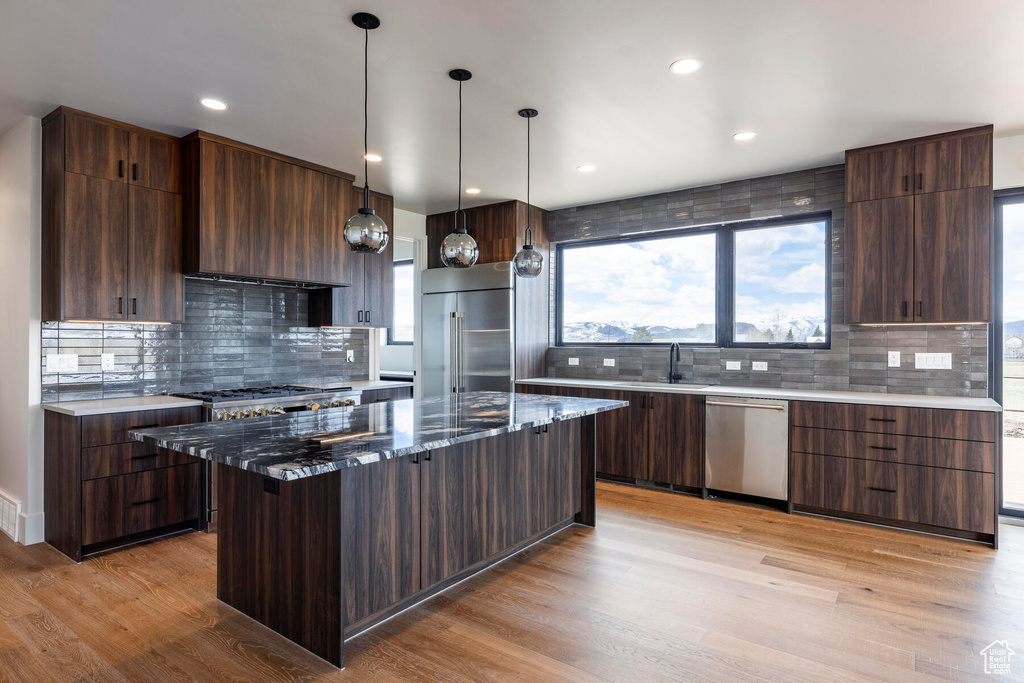 Kitchen featuring decorative backsplash, a kitchen island, light wood-type flooring, appliances with stainless steel finishes, and dark stone countertops