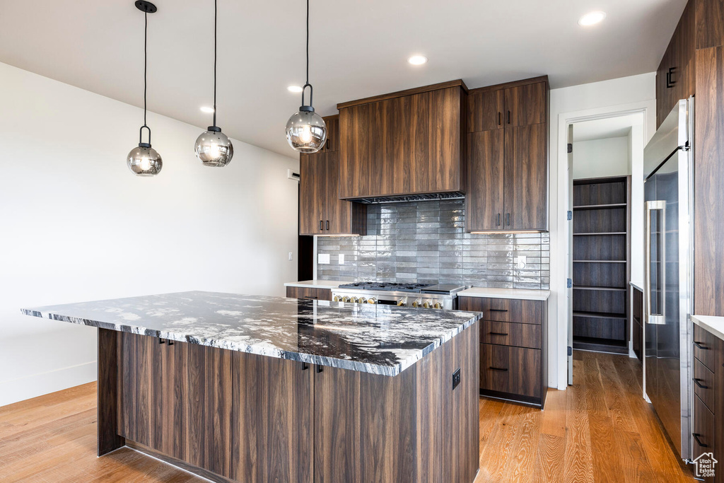 Kitchen featuring appliances with stainless steel finishes, tasteful backsplash, dark stone countertops, hanging light fixtures, and light hardwood / wood-style flooring