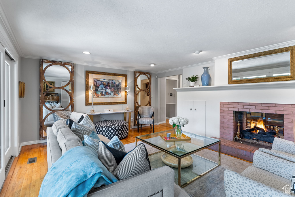 Living room featuring ornamental molding, a brick fireplace, and light wood-type flooring