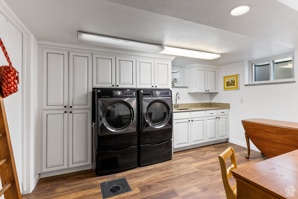 Clothes washing area with cabinets, sink, light hardwood / wood-style flooring, and washing machine and clothes dryer