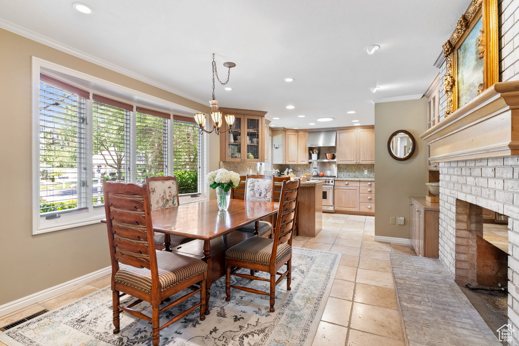 Tiled dining space featuring ornamental molding, a notable chandelier, and a brick fireplace