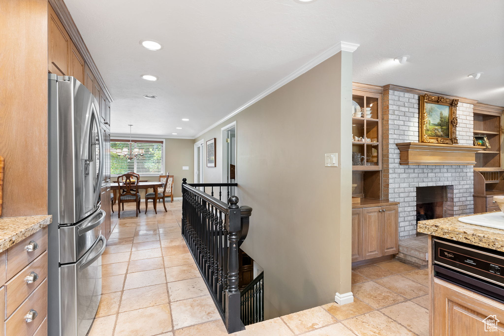 Kitchen featuring ornamental molding, light tile patterned flooring, stainless steel refrigerator with ice dispenser, and a fireplace