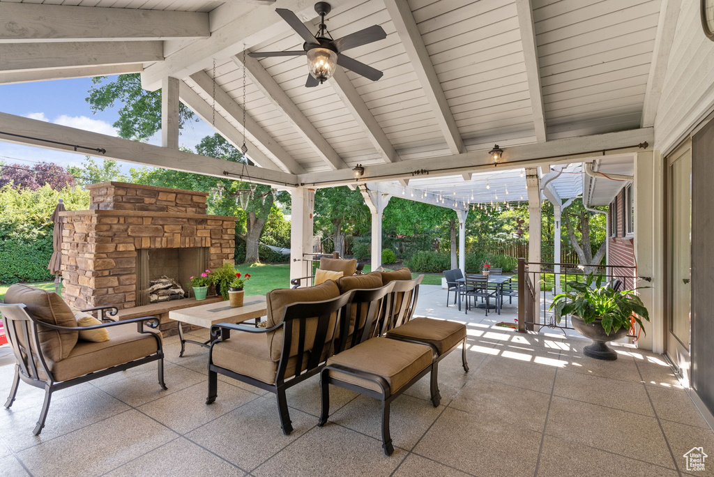 Sunroom / solarium with an outdoor stone fireplace, ceiling fan, and vaulted ceiling with beams