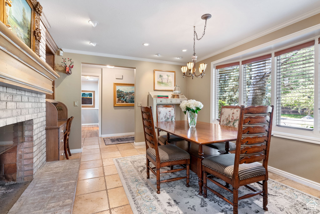 Dining space featuring a chandelier, a fireplace, light tile patterned floors, and ornamental molding