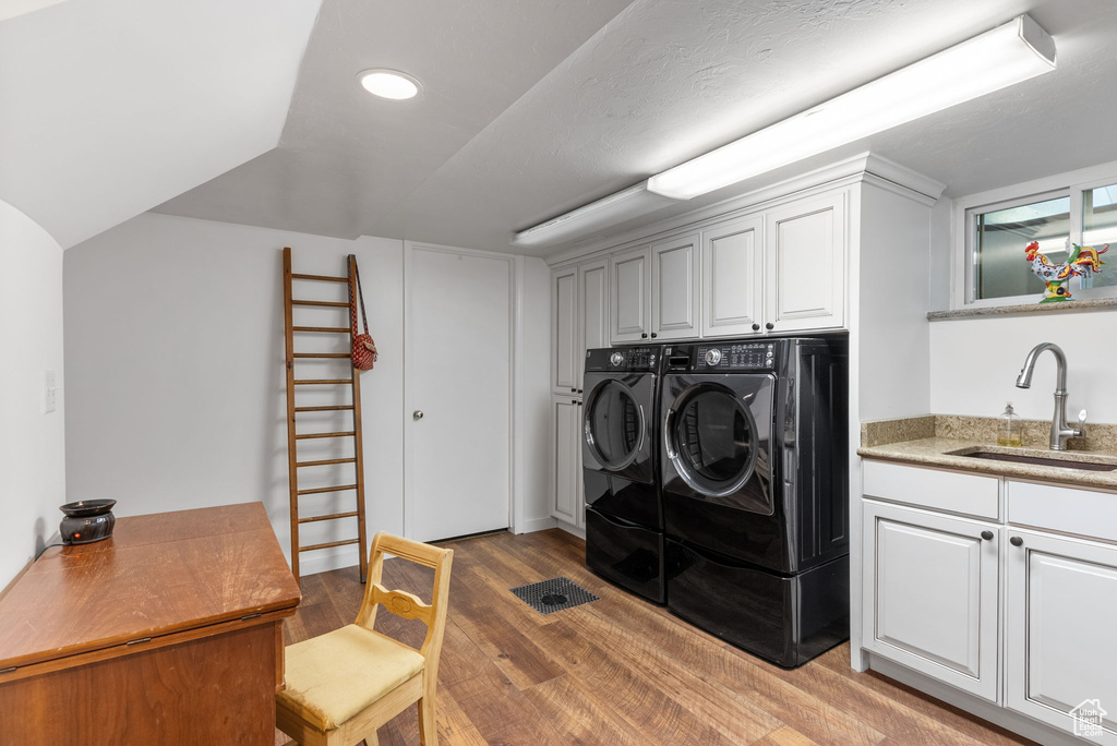 Washroom featuring cabinets, wood-type flooring, washing machine and dryer, and sink