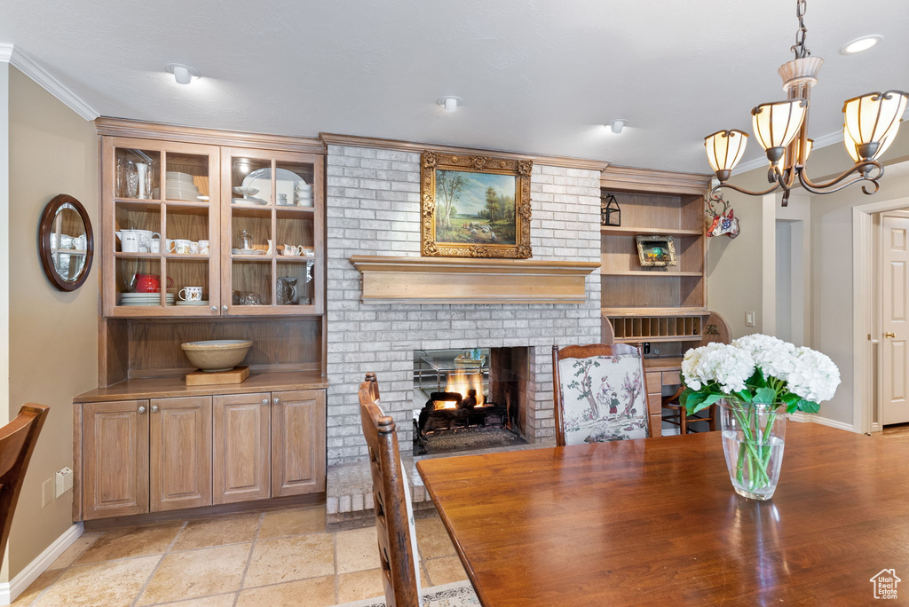 Dining space featuring light tile patterned floors, an inviting chandelier, brick wall, a fireplace, and ornamental molding