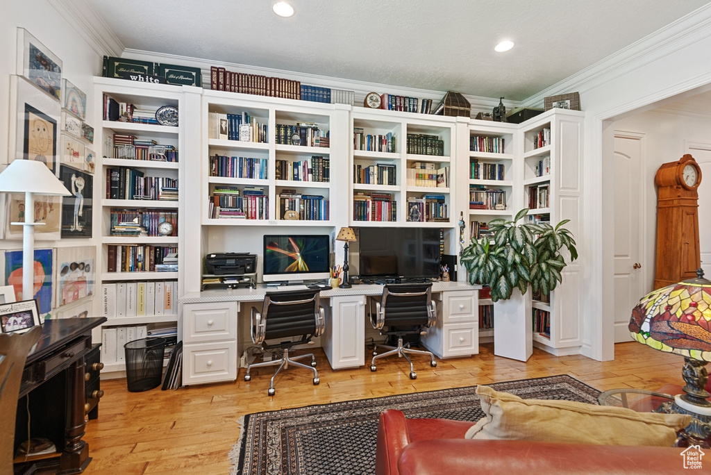 Office with built in desk, ornamental molding, and light hardwood / wood-style floors