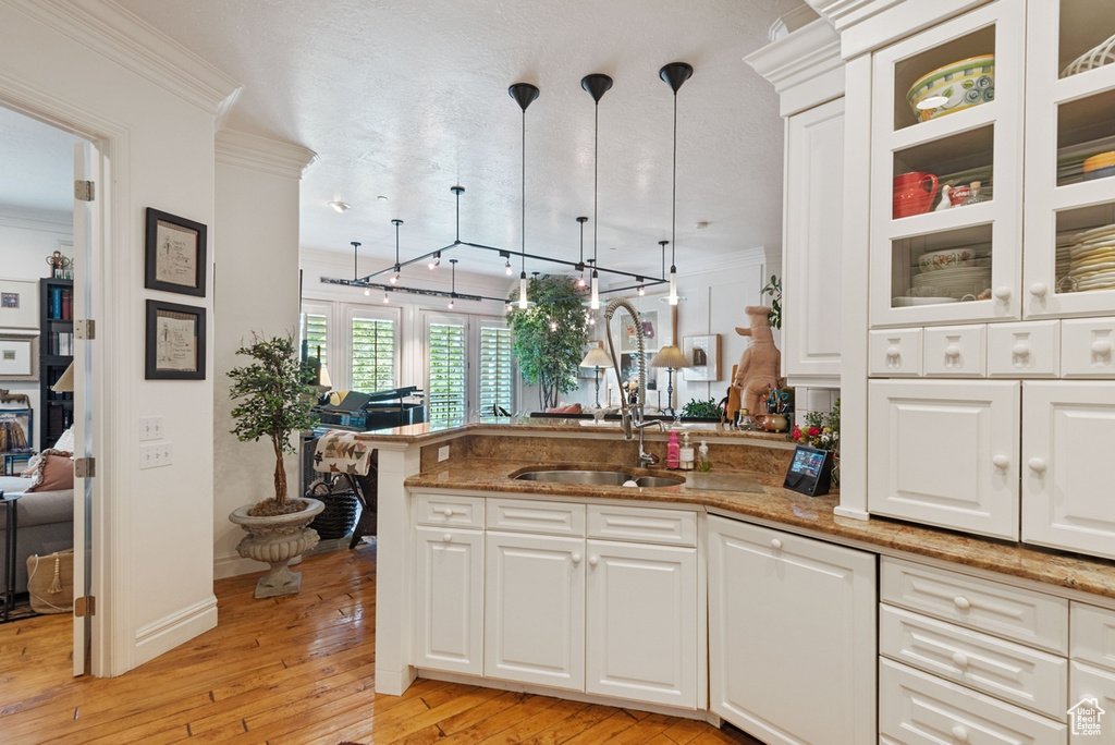 Kitchen with decorative light fixtures, sink, white cabinetry, and stone countertops