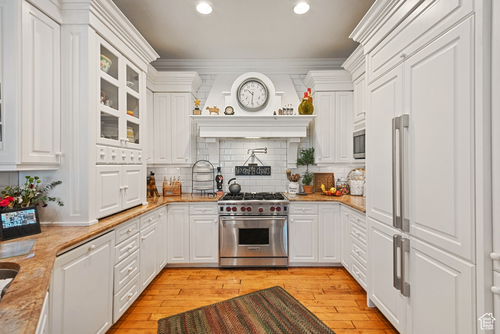 Kitchen featuring built in appliances, light hardwood / wood-style flooring, tasteful backsplash, and white cabinetry