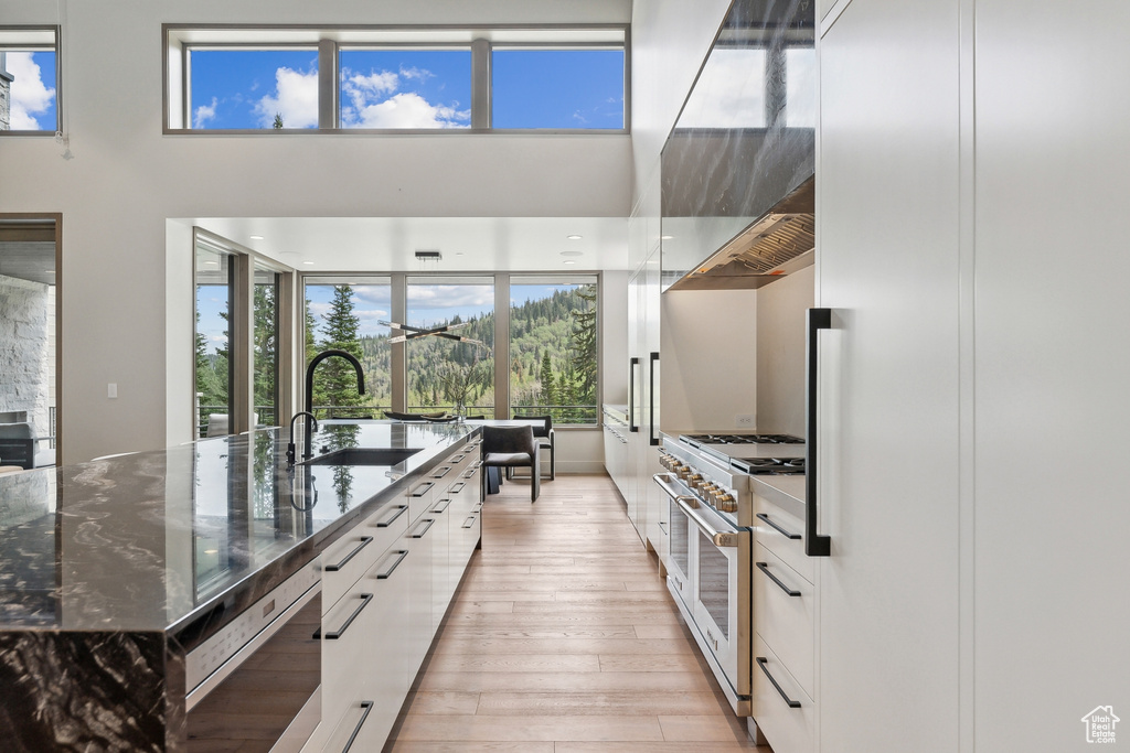 Kitchen featuring range with two ovens, white cabinets, dark stone countertops, a center island with sink, and light hardwood / wood-style floors