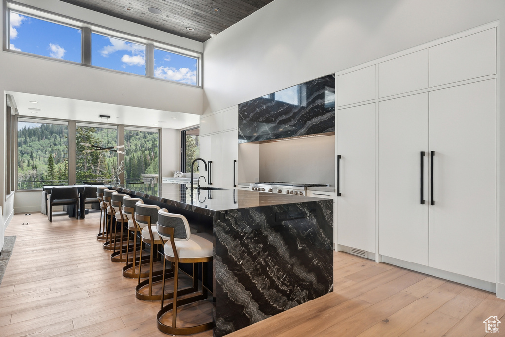 Kitchen featuring white cabinets, light hardwood / wood-style floors, a center island with sink, and sink